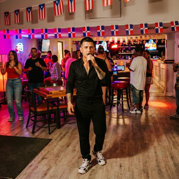 Singer performs before patrons in a lively Puerto Rican-themed restaurant and bar decorated with flags and colorful lighting.