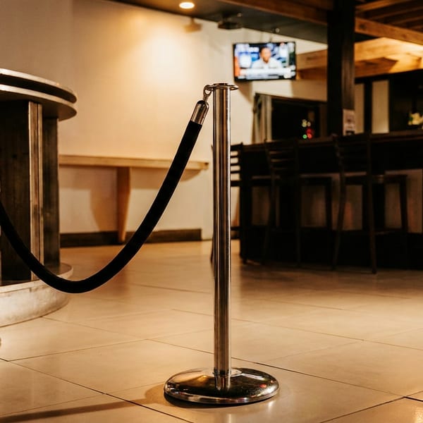 Warmly lit restaurant interior with velvet ropes, polished tile floors, high-top tables, bar seating, and a wall-mounted television.