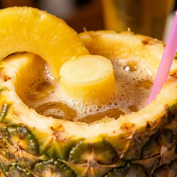 Pineapple cocktail filled with frothy golden drink, topped with pineapple slices and served with a pink straw.