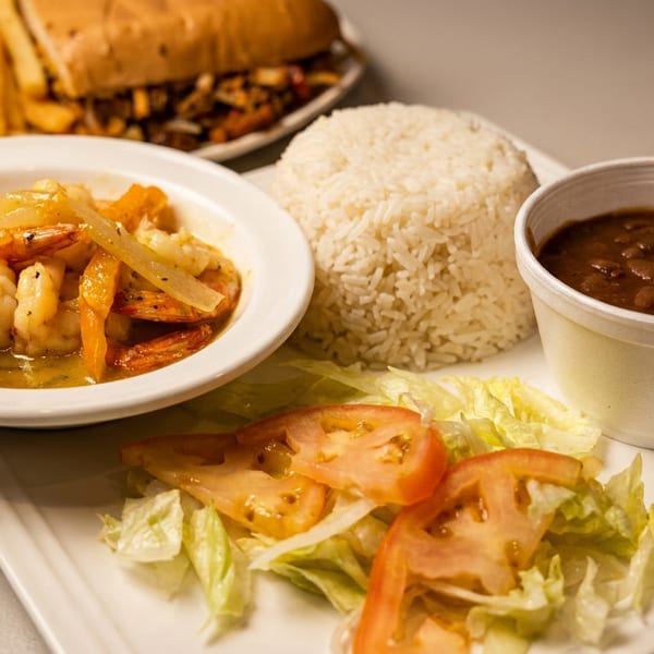 Tray featuring saucy shrimp, white rice, black beans, lettuce and tomato salad, with a burger and fries in the background.